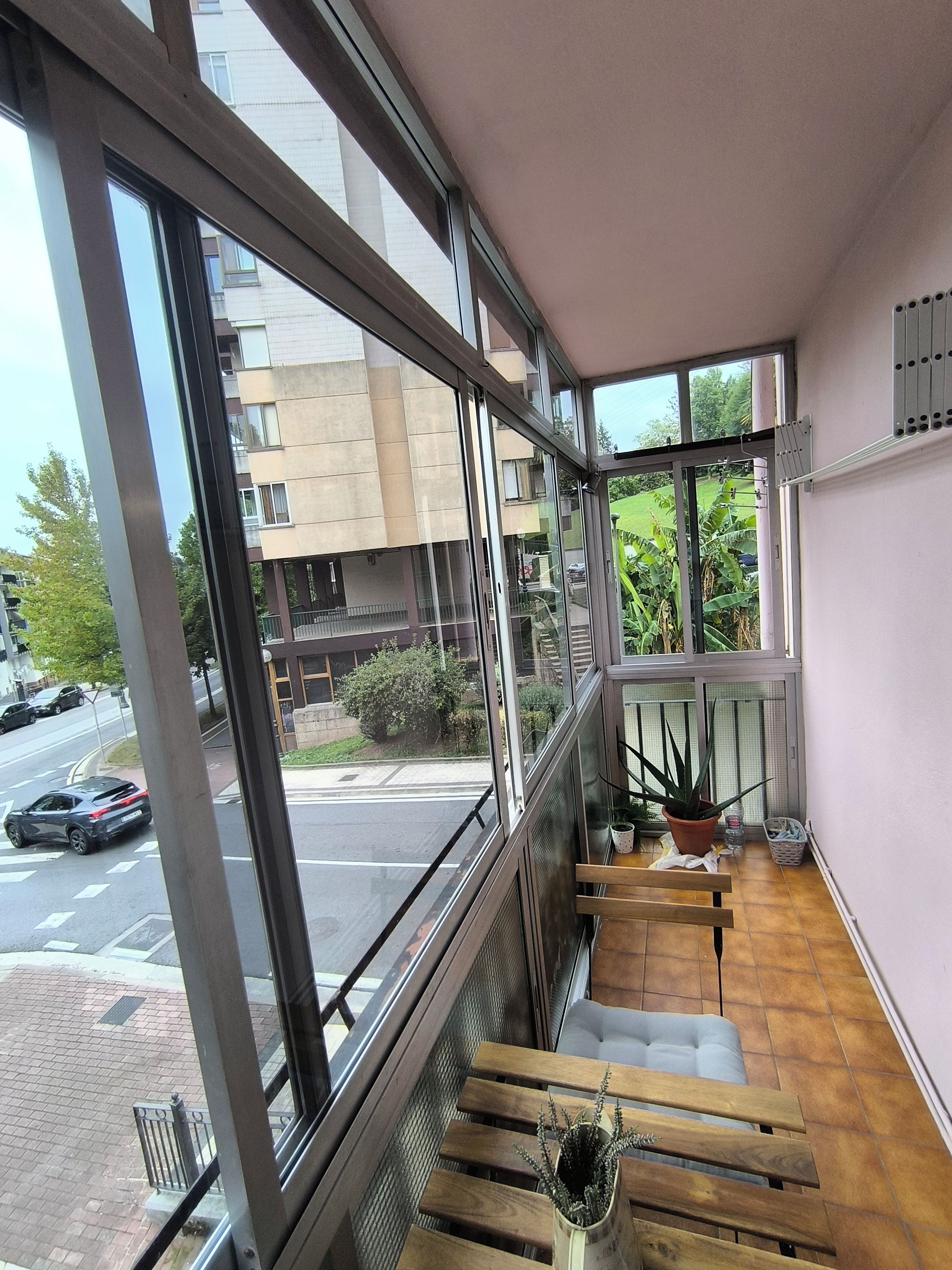 A balcony with a view of a street, a potted plant, and a wooden bench.
