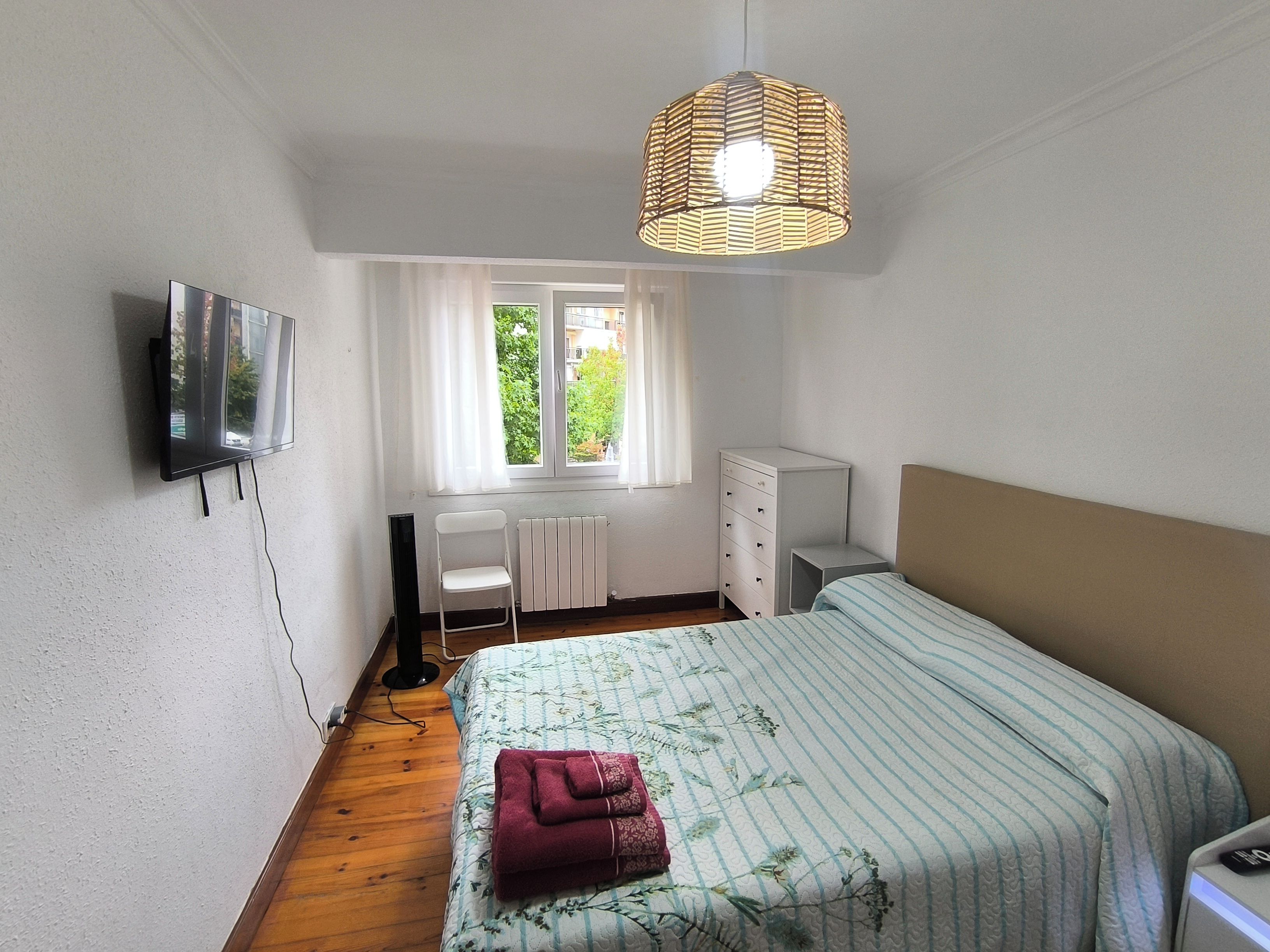 A bedroom with a bed, a radiator, a chair, a dresser, and a television on the wall.