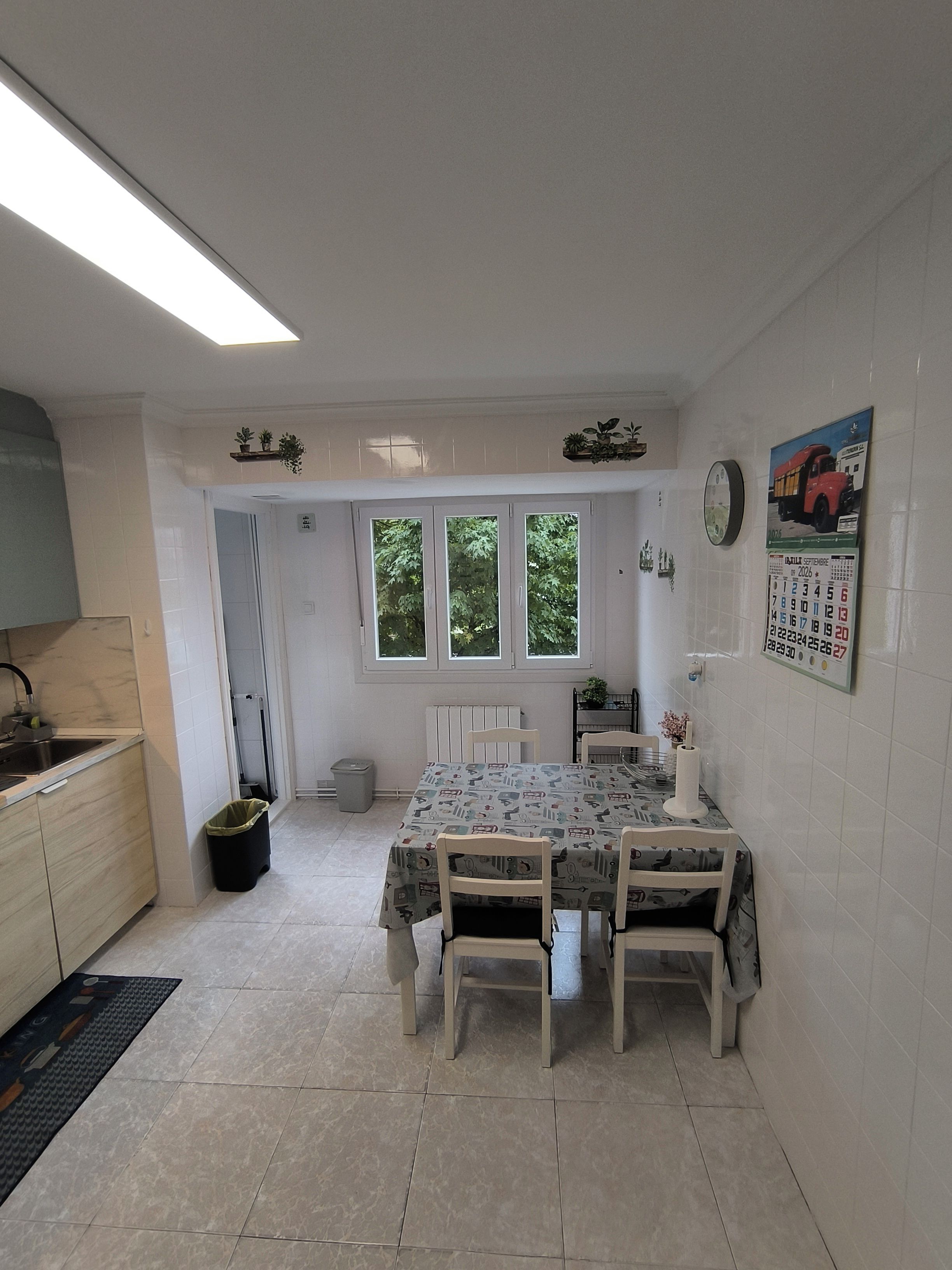 Une cuisine avec une table à manger, des chaises, une horloge et un calendrier accroché au mur.