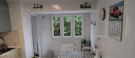 A kitchen with a dining table, chairs, a clock, and a calendar on the wall.