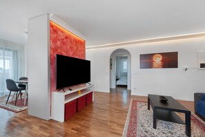 A modern living room with a flat-screen TV, a red accent wall, a dining area with a table and chairs, and a hallway leading to a bedroom. - Apartment 'Casa della Luna' (Lecce)
