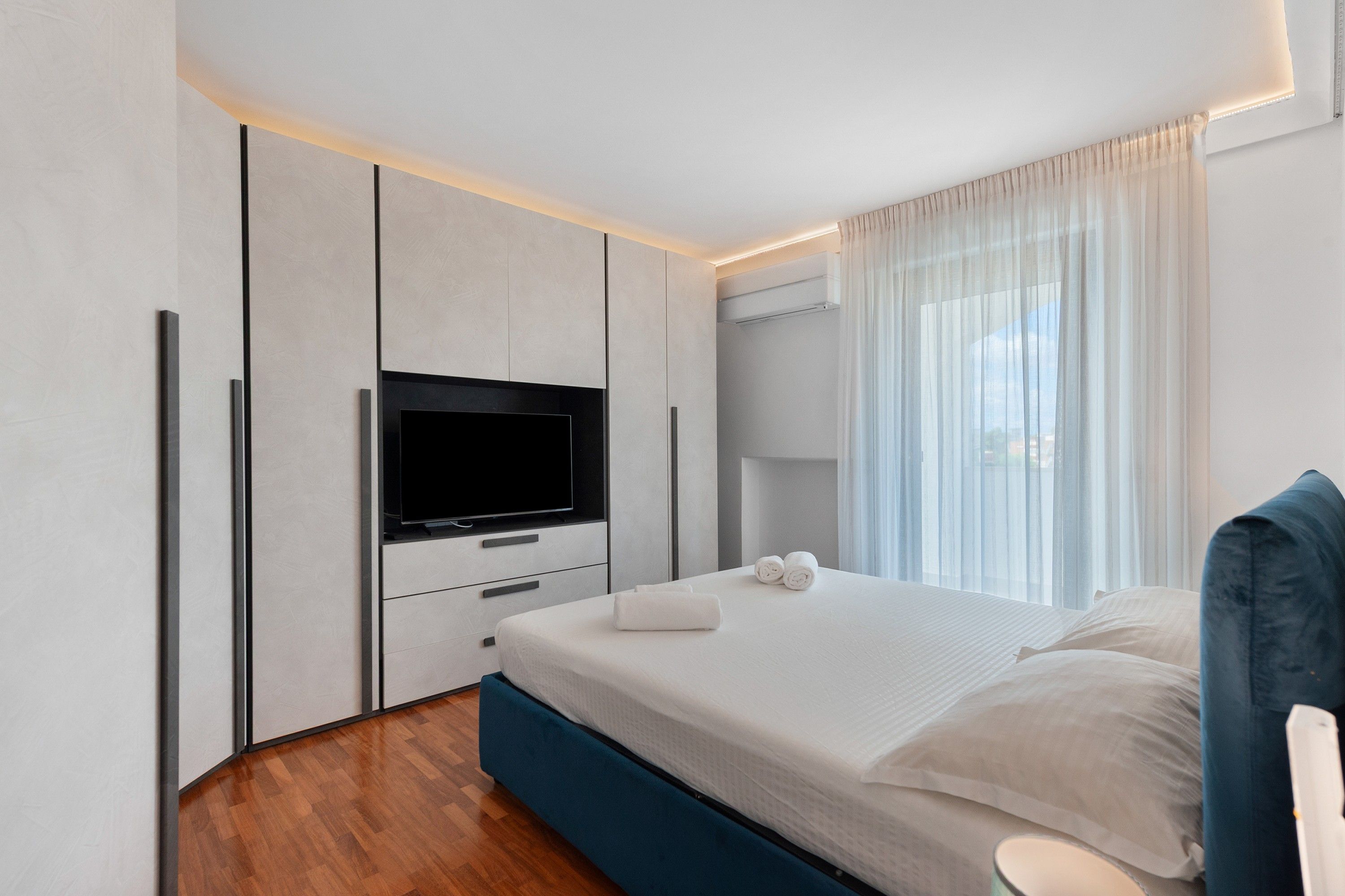 A modern bedroom with a flat-screen TV, a bed with white linens, and a wooden floor.
