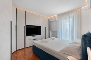 A modern bedroom with a flat-screen TV, a bed with white linens, and a wooden floor. - Apartment 'Casa della Luna' (Lecce)