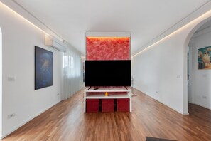 A hallway with a flat-screen TV on a white stand, wooden flooring, and artwork on the walls. - Apartment 'Casa della Luna' (Lecce)