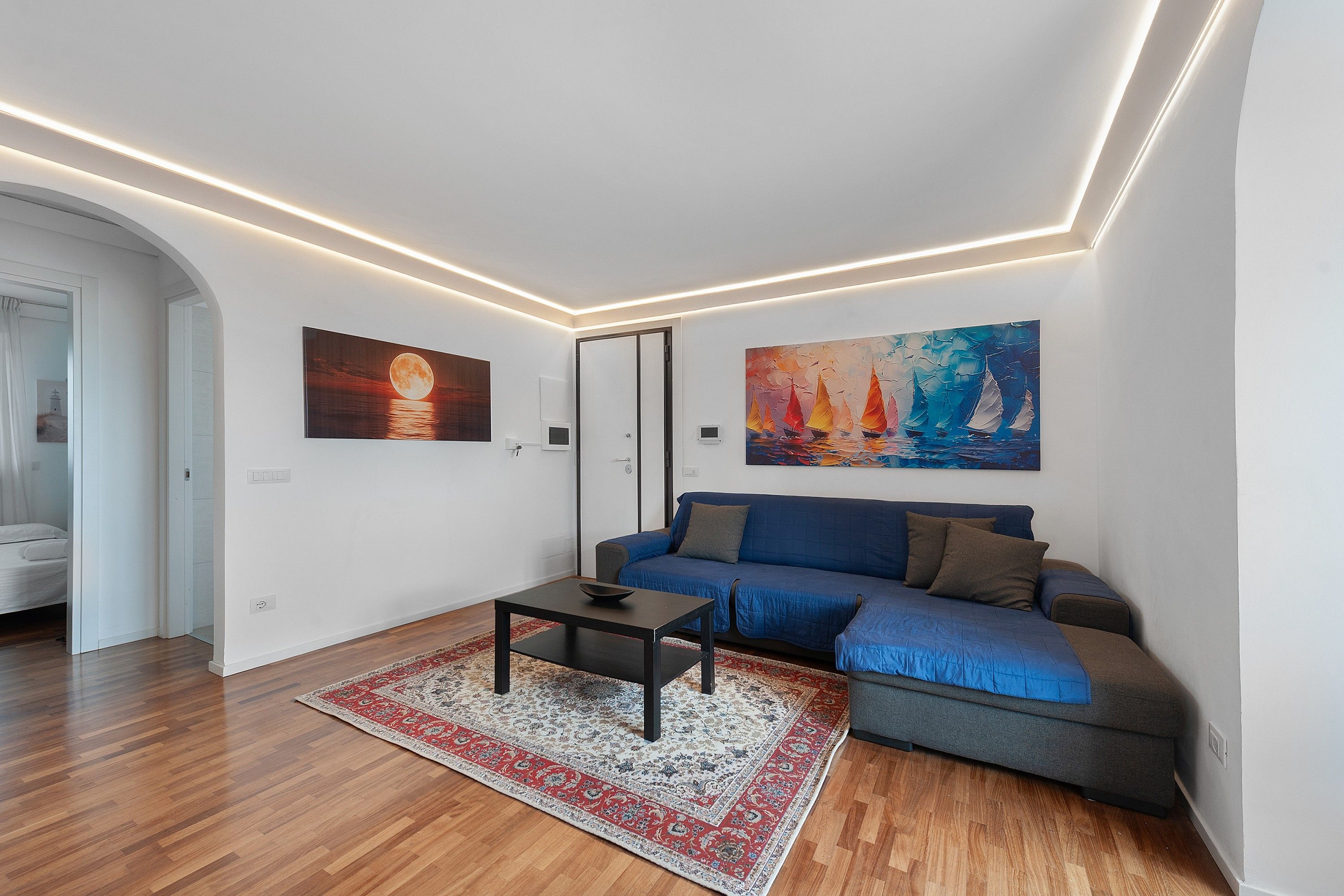 Uma sala de estar moderna com um sofá azul, uma mesa de centro e duas pinturas na parede.