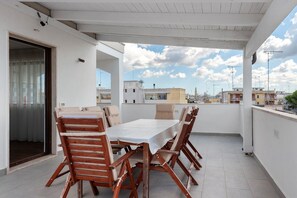 A covered outdoor dining area with a table and chairs, a door, and a view of the cityscape. - Apartment 'Casa della Luna' (Lecce)