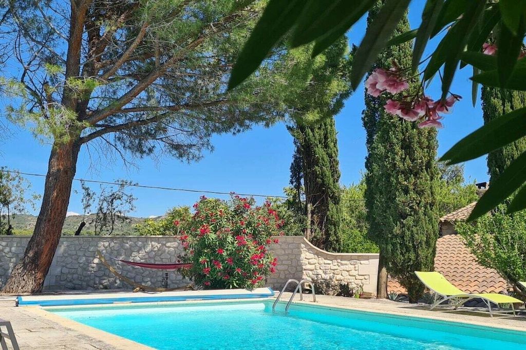Une piscine bordée d’un mur en pierre, un hamac et une vue sur le paysage environnant.