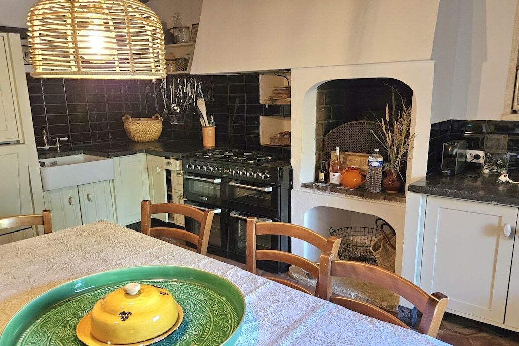 Una cocina con estufa, horno y varios utensilios. Hay una mesa de comedor con sillas y una bandeja verde.