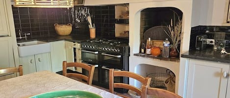 Una cocina con estufa, horno y varios utensilios. Hay una mesa de comedor con sillas y una bandeja verde.