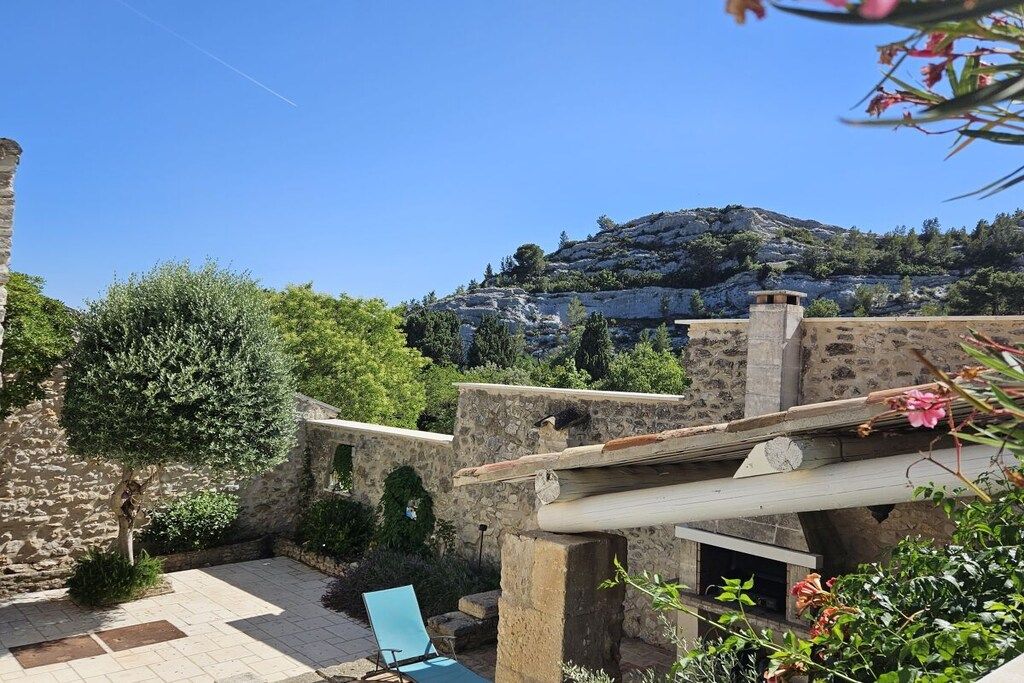 Ein gepflasterter Innenhof mit blauem Stuhl, einer Pergola und Blick auf einen Hügel mit Gebäuden.