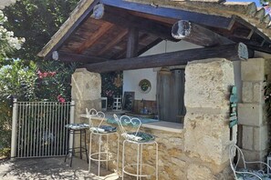 A stone patio with a wooden pergola, a metal gate, and three white metal chairs with patterned cushions. - Mas de L" Embeli with Pool (Mouries)