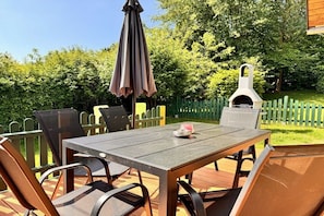 An outdoor patio with a table and chairs, a grill, and a green fence. - The Fox's Den - Log Cabin 3 (Bad Sachsa \/ OT Steina)