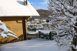A snow-covered wooden house with a white roof, a wooden fence, and a snow-laden tree in the foreground. - The Fox's Den - Log Cabin 3 (Bad Sachsa \/ OT Steina)