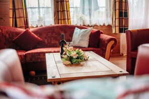 A cozy living room with a red sofa, a wooden coffee table with a floral arrangement, and a bottle of wine. - The Fox's Den - Log Cabin 3 (Bad Sachsa \/ OT Steina)
