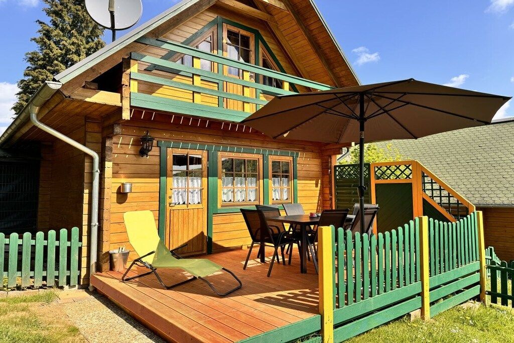 A wooden cabin with a deck, outdoor seating, and a covered patio area.