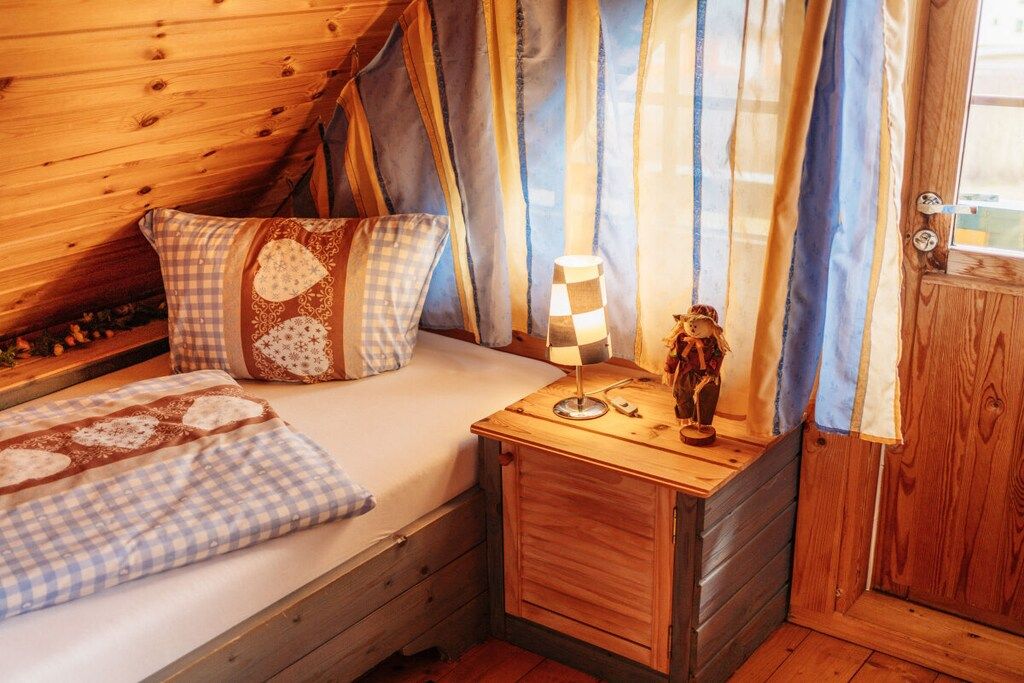 Un dormitorio acogedor con una cama de madera, ropa de cama a cuadros, una lámpara de noche y un pequeño adorno.