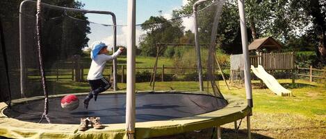 Un trampolín con red de seguridad, rodeado de césped y árboles.