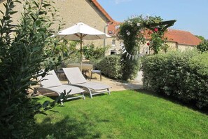 Ein Garten mit Rasen, zwei Liegestühlen, einem Tisch und einem weißen Sonnenschirm.