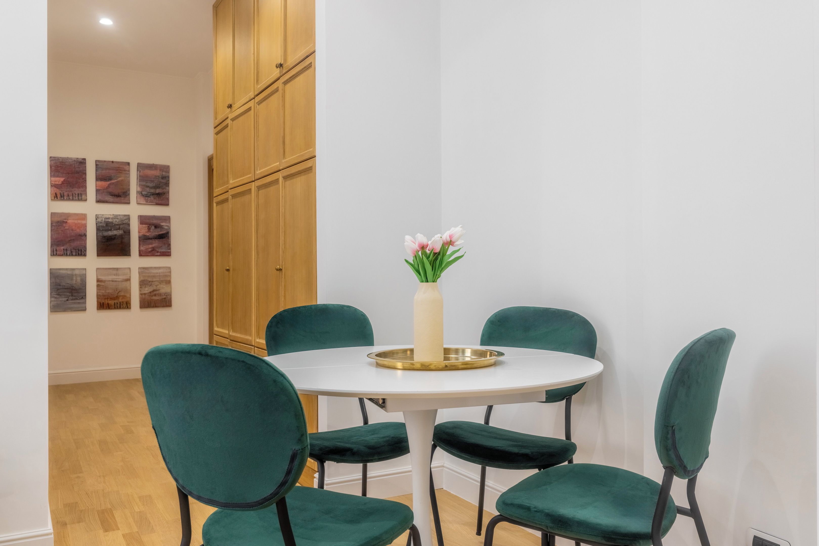 A dining area with a round table, four green chairs, and a vase with flowers.