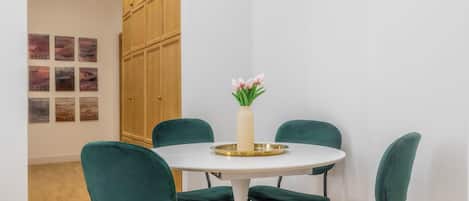 A dining area with a round table, four green chairs, and a vase with flowers.