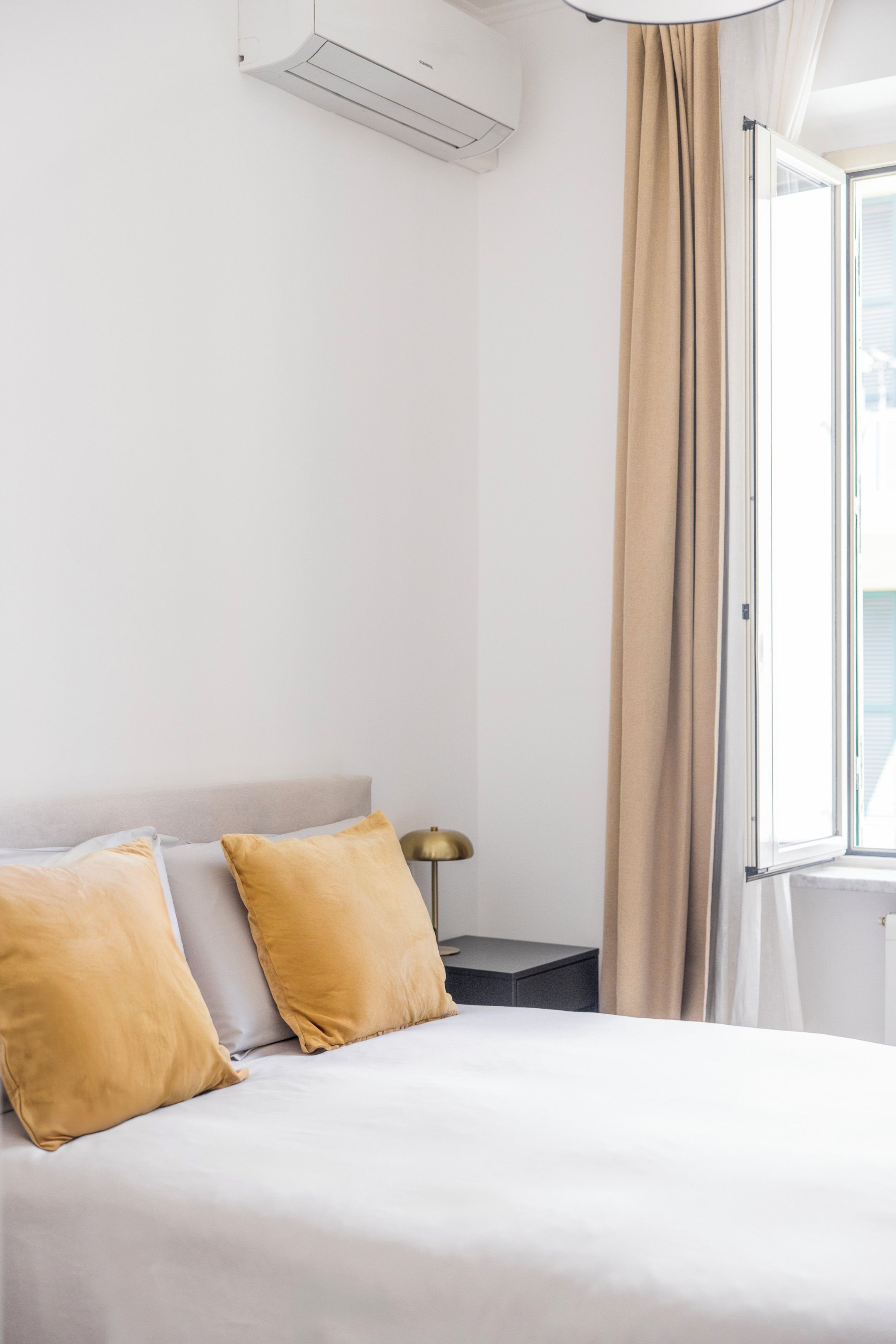 A hotel room with a bed, two pillows, a bedside table with a lamp, and a window with curtains.