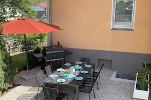 An outdoor patio with a table set for dining, a grill, and a red umbrella. - The Fox's Den - SweetDreams (Bad Sachsa)
