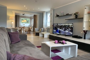 A modern living room with a sofa, coffee table, and a television displaying a conference. - The Fox's Den - SweetDreams (Bad Sachsa)