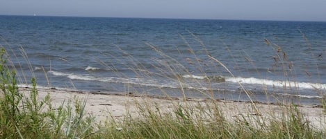 Ein Strand mit Wellen, Seegras und Gras im Vordergrund.