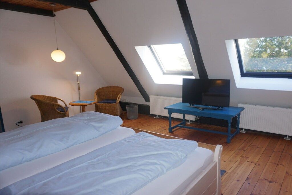 Een kamer met een bed, een televisie op een blauwe tafel, twee rieten stoelen en een dakraam.