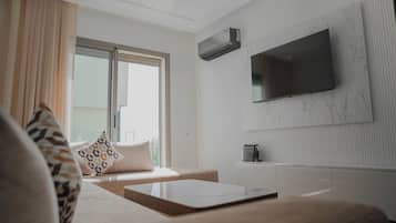 A modern living room with a sofa, a coffee table, a flat-screen TV mounted on a marble wall, and a window with curtains.