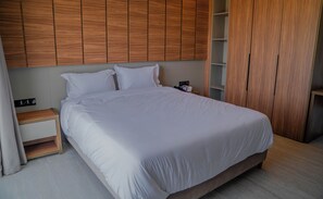 A neatly made bed with white linens in a modern room with wooden paneling on the walls and a wooden wardrobe.