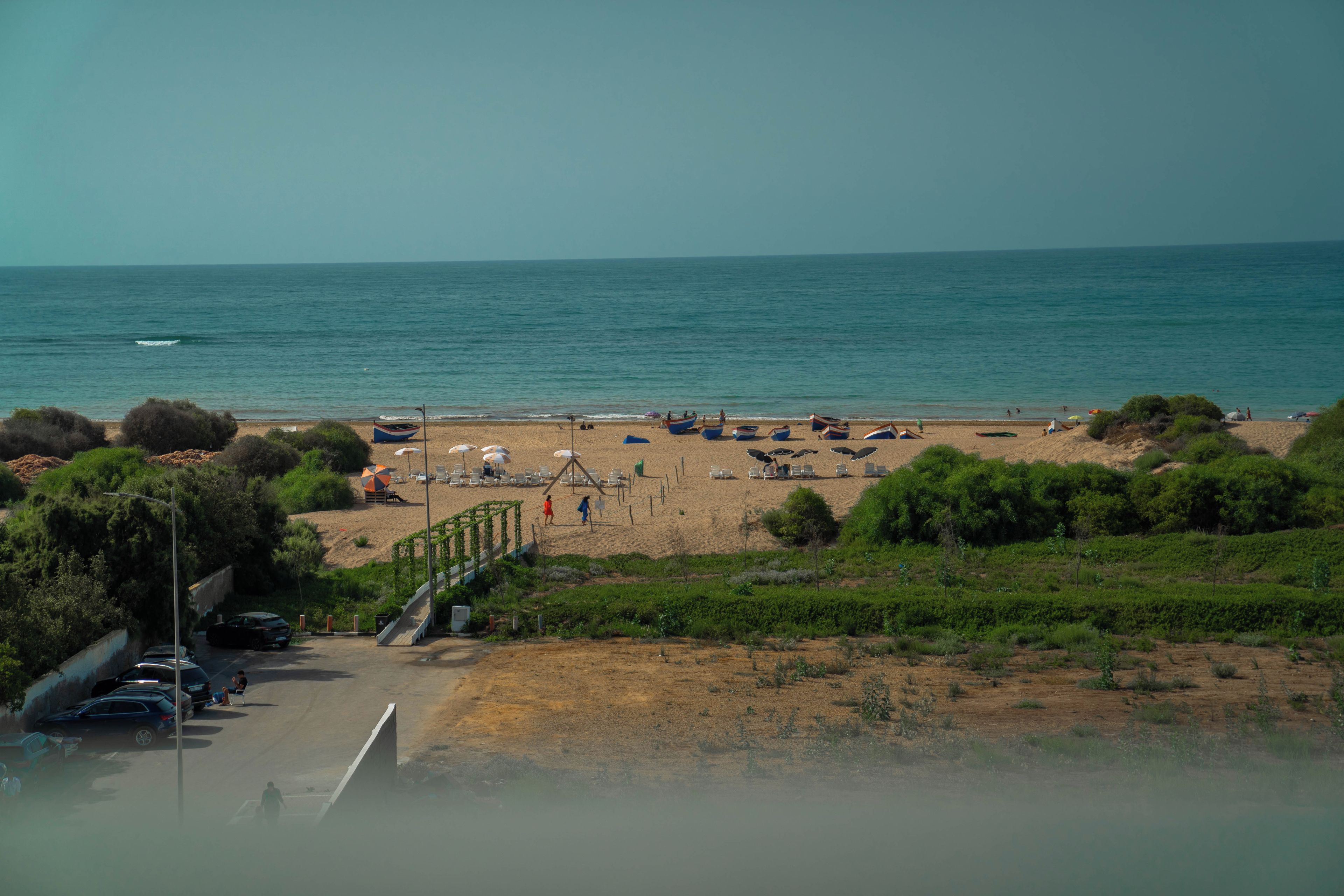 Ein Strand mit Booten, Sonnenschirmen und einem Parkplatz.