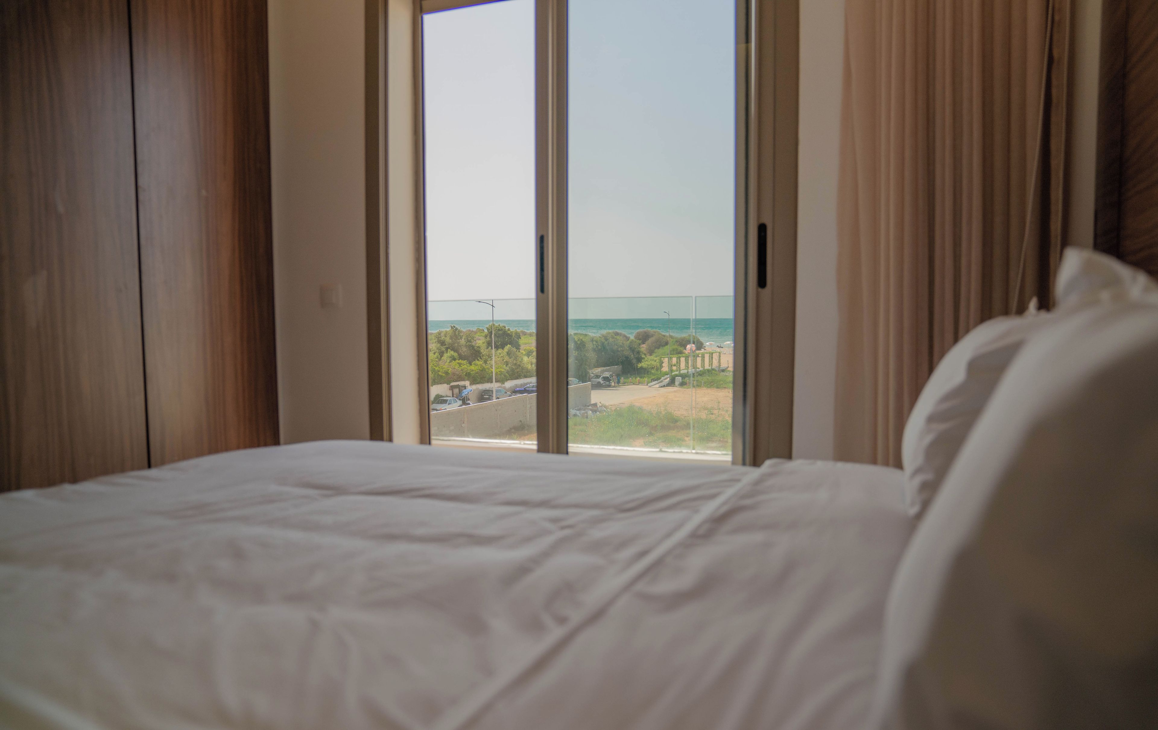A bedroom with a large window, a bed, and a view of the beach.