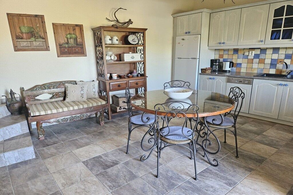 A dining area with a round table and chairs, a sofa, a cabinet with decorative items, and a kitchen area with cabinets and appliances.
