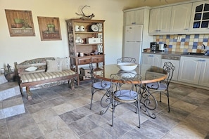 A dining area with a round table and chairs, a sofa, a cabinet with decorative items, and a kitchen area with cabinets and appliances. - Villa in Pitsidia with swimming pool (Pitsidia)