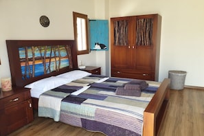 A bedroom with a wooden headboard, a quilted bedspread, a bedside table with a lamp, and a wardrobe with a rustic design. - Villa in Pitsidia with swimming pool (Pitsidia)