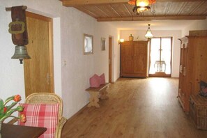 Ein Zimmer mit Holzboden, Holztür, Korbstuhl, kleinem Tisch mit Kissen und einer hängenden Glocke.