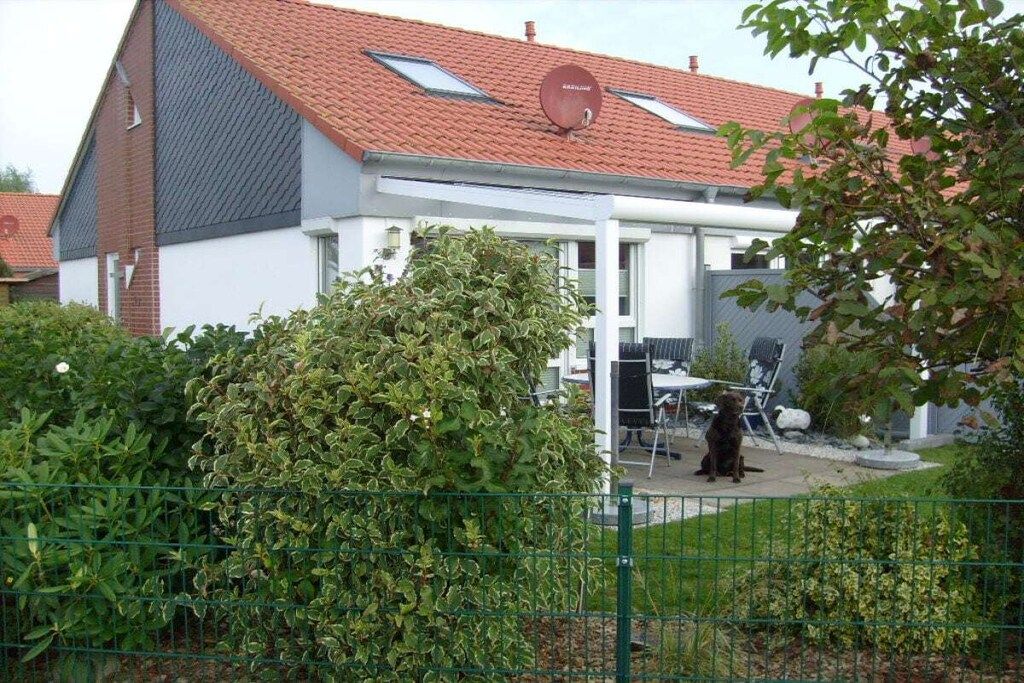 Une maison avec un toit recouvert de tuiles rouges, une antenne parabolique et une cour clôturée où se trouve un chien.