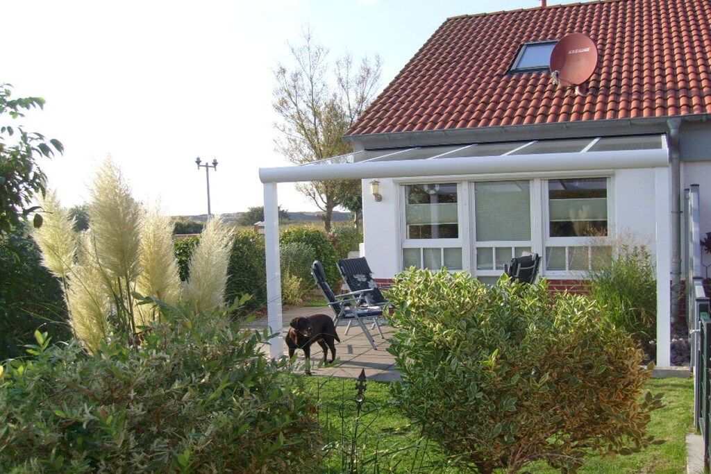 A house with a red-tiled roof, a satellite dish, and a covered patio area with chairs.