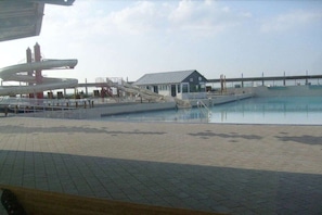 A swimming pool area with a water slide, a small building, and a dock extending into the water. - Holiday home with 1 bedroom (Wurster Nordseeküste)