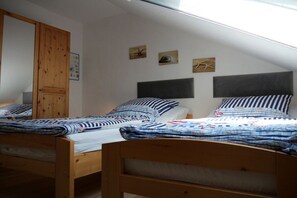 A dormitory room with two wooden bunk beds, a wooden wardrobe, and a sloped ceiling with skylights. - Holiday home with 1 bedroom (Wurster Nordseeküste)