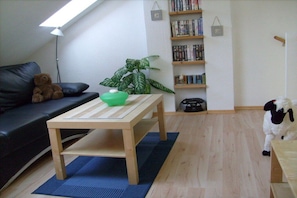 Een woonkamer met een bank, een tafel met een schaal en een plant, een boekenkast, en een hond.