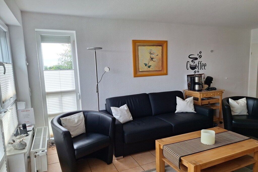 Een woonkamer met een zwarte bank, een bijzettafeltje en een koffieapparaat.