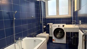 Un bagno moderno con una vasca da bagno, una lavatrice e una finestra.