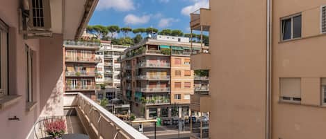 A balcony with a table and chairs, overlooking a street with parked cars and buildings.