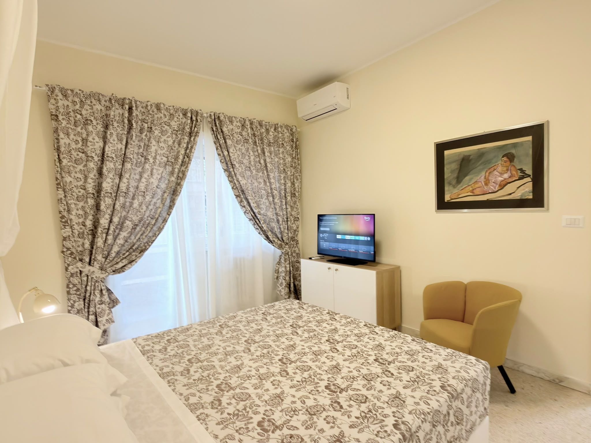 Una camera d'albergo con un letto, una televisione, un quadro appeso e una sedia.