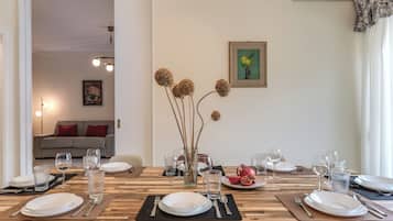 Zona pranzo con tavolo in legno apparecchiato per un pasto, un vaso con fiori secchi e un quadro appeso al muro.