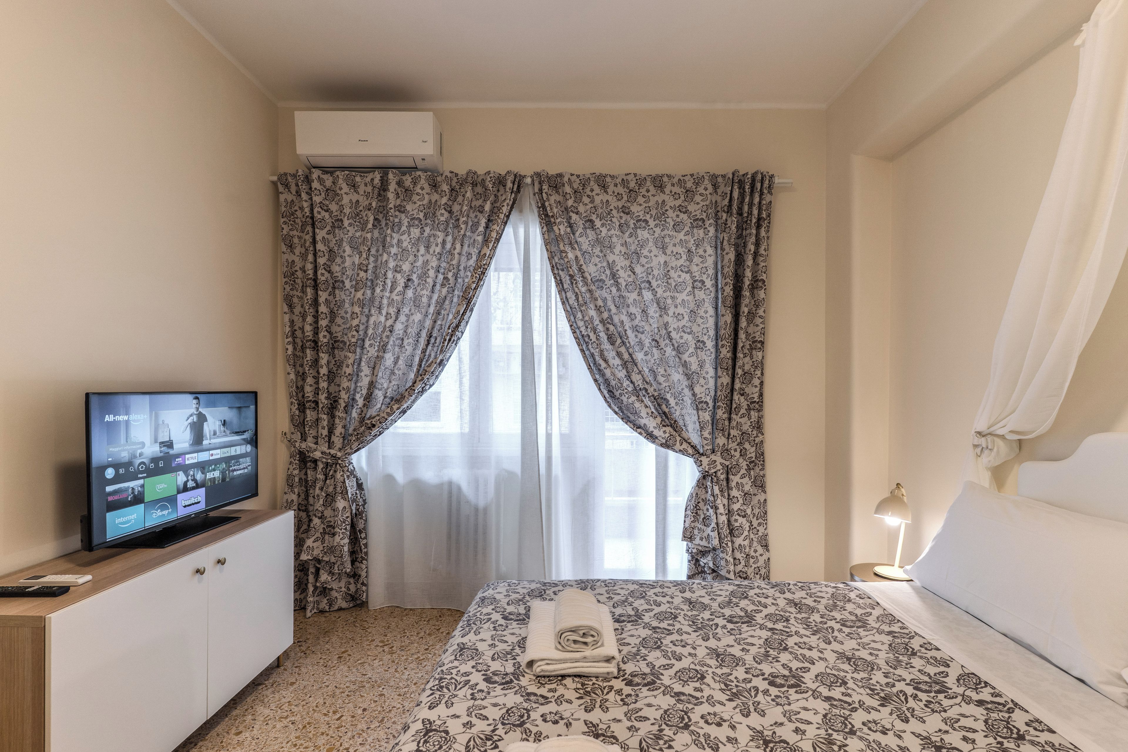 Een hotelkamer met een bed, gordijnen, een televisie en een bedlamp.