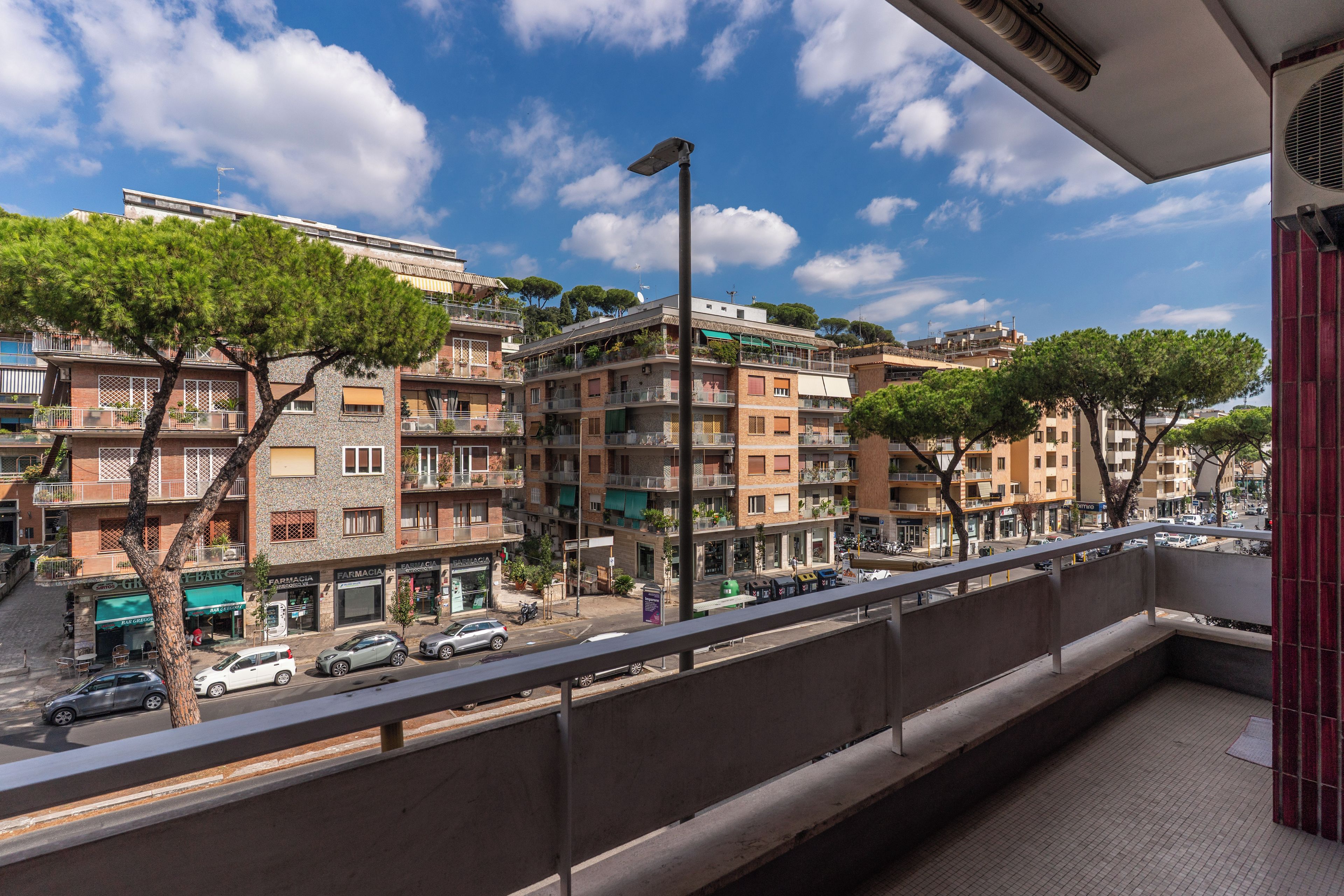 A balcony with a view of a street lined with multi-story buildings, some with balconies and greenery.