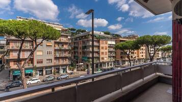 A balcony with a view of a street lined with multi-story buildings, some with balconies and greenery.